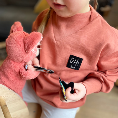 Kind beim spielen, dass einen rostfarbenen Sweater mit OH! kid Aufnäher auf der Brust trägt und die passenden Patches dazu in der Hand hält.